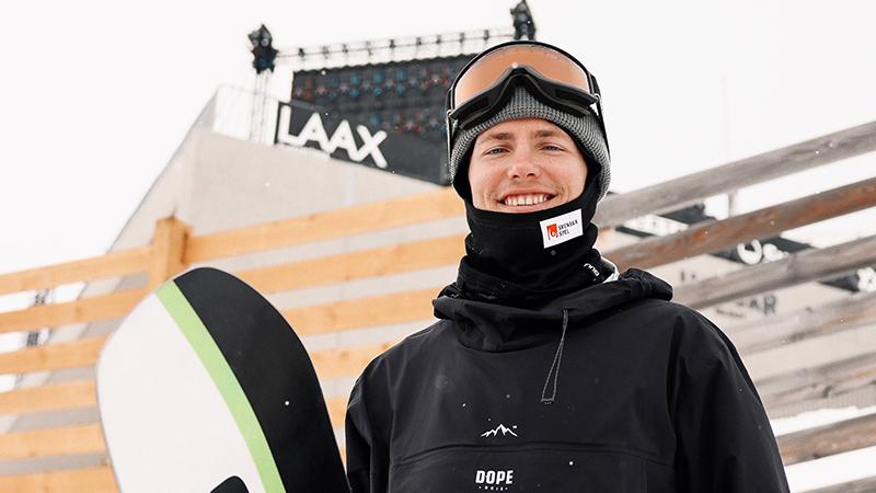 Sven Thorgren står i backen och håller i sin snowboard med ett brett leende. 